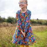 A child wearing a Frugi Organic Cotton Sofia Skater Dress in a Navy with a Retro Floral print with yellow leggings.
