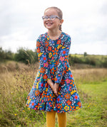 A child wearing a Frugi Organic Cotton Sofia Skater Dress in a Navy with a Retro Floral print with yellow leggings.