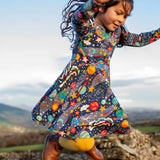 Child wearing the Frugi Sofia organic cotton skater dress in navy with an all over explore the stars print with yellow tights and brown boots. 