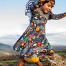 Child wearing the Frugi Sofia organic cotton skater dress in navy with an all over explore the stars print with yellow tights and brown boots. 