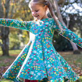 A child wearing the Frugi Sofia skater dress with a wild woods print. A beautiful turquoise blue with a pattern all over featuring flowers, greenery and mushrooms.
