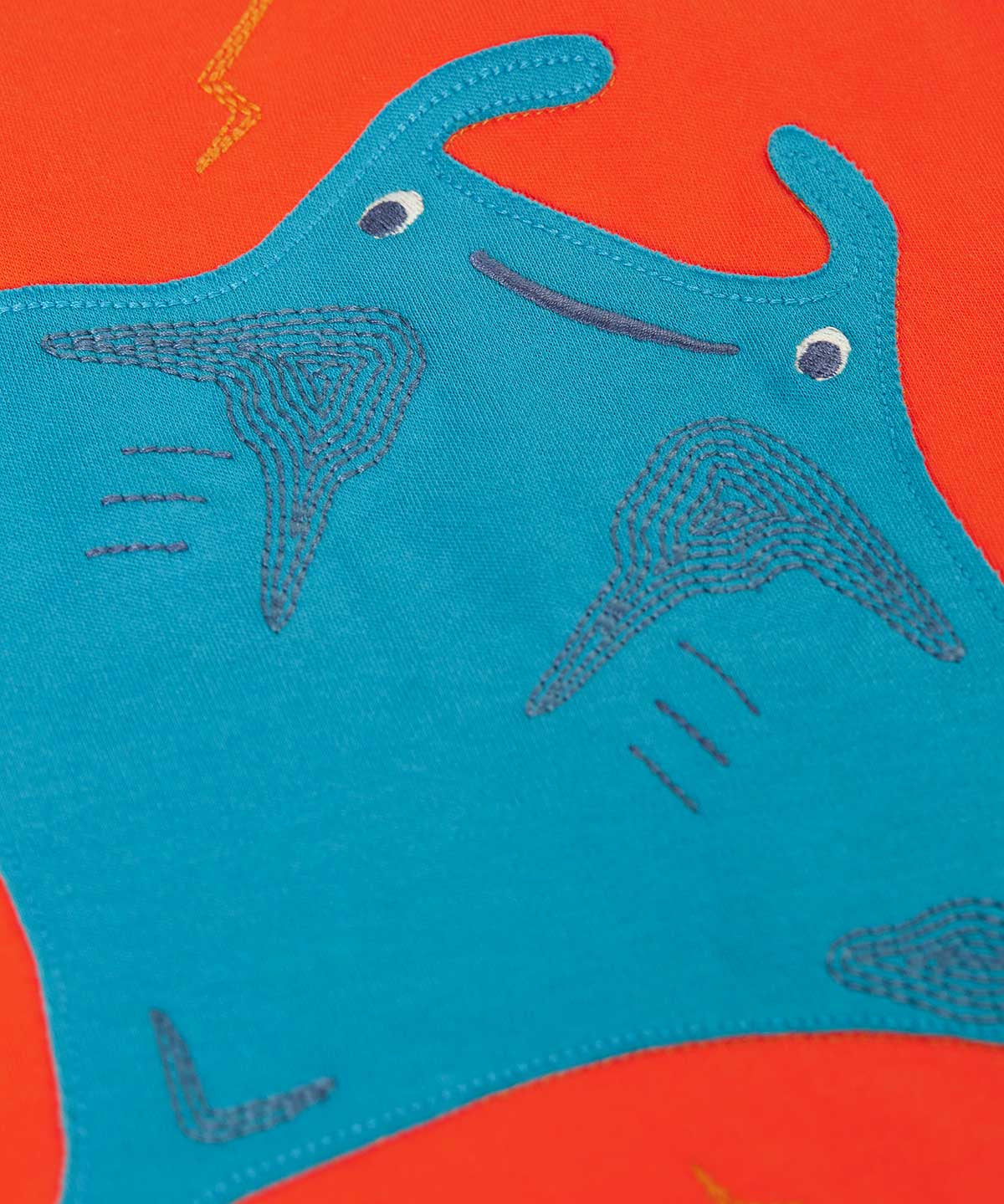 A super close up of the ray on the front of the Frugi orange children's jumper. The blue ray has embroidered details on it.