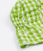 A close up of the Frugi little seersucker sun hat. Showing the elastic on the back of hat in between the neck protector and top panel of the hat with the Frugi label on the side on white and green gingham organic cotton fabric