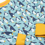 Frugi long sleeved organic cotton sundown pyjamas with a penguin waddle print. The pajamas have a yellow gold coloured neckline and cuffs.