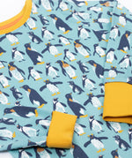 Frugi long sleeved organic cotton sundown pyjamas with a penguin waddle print. The pajamas have a yellow gold coloured neckline and cuffs.