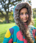 A child wearing the Frugi kids penhale super spot parka outside showing the furry hood detail and the big circles design on light blue organic cotton fabric. 