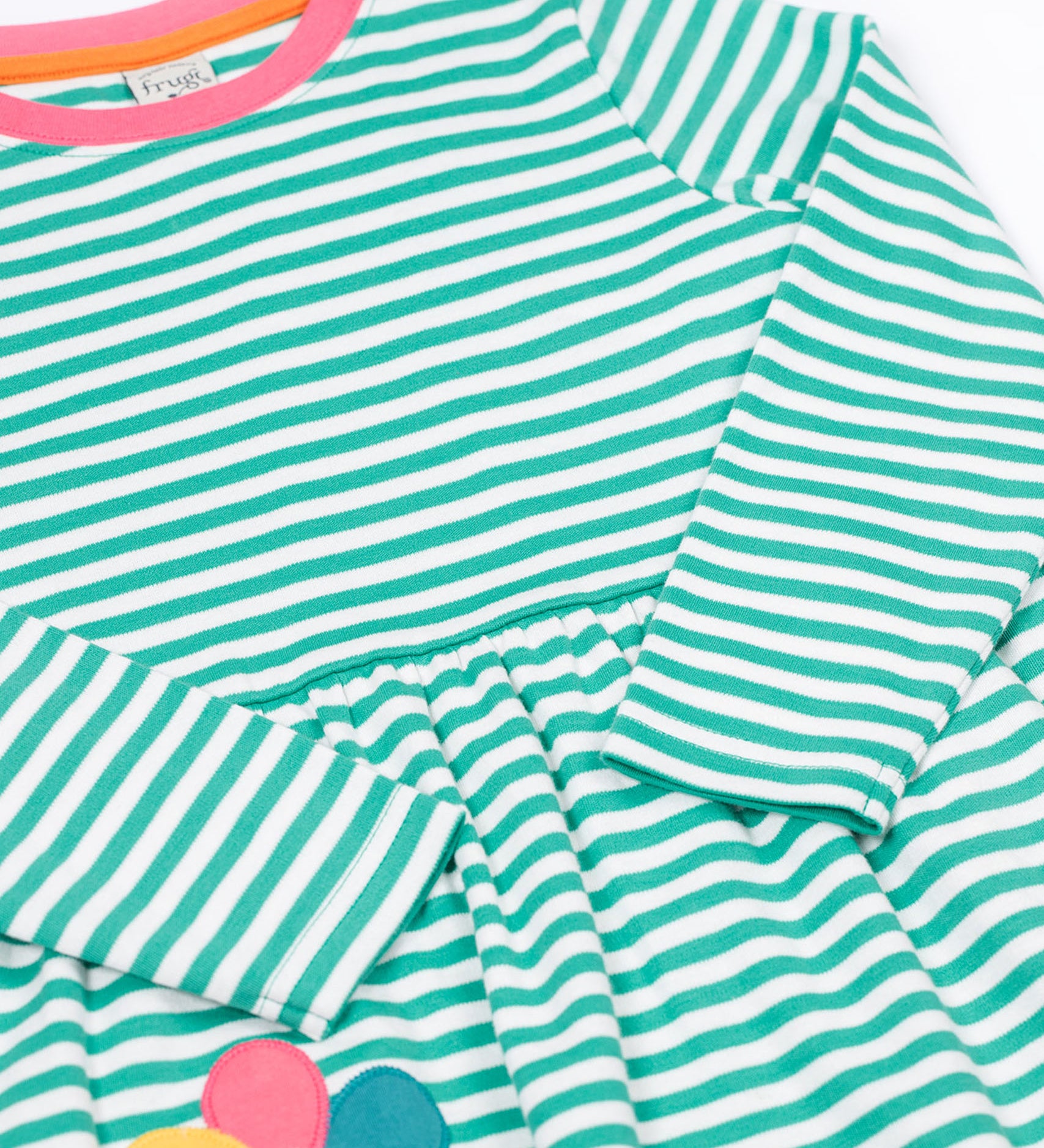 A close up of the Frugi kids tammy dress in dragon stripes/flowers showing the long sleeve and pink trim detail on striped organic cotton fabric.
