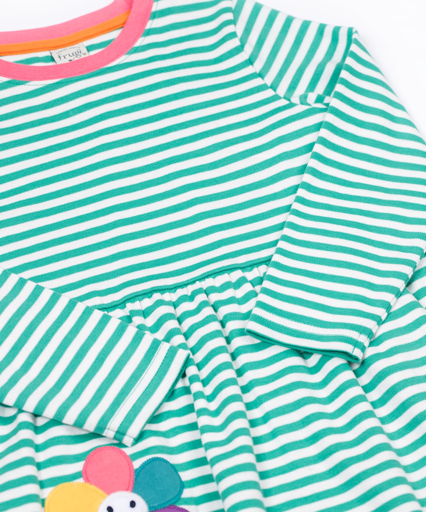 A close up of the Frugi kids tammy dress in dragon stripes/flowers showing the long sleeve and pink trim detail on striped organic cotton fabric.