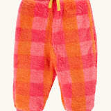 A pair of frugi fuzzy, plush jogger-style pants in a pink and orange plaid pattern, featuring a yellow drawstring bow at the waist and ribbed cuffs at the ankles.