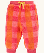 A pair of frugi fuzzy, plush jogger-style pants in a pink and orange plaid pattern, featuring a yellow drawstring bow at the waist and ribbed cuffs at the ankles.