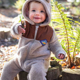 A child sitting on a log wearing the Frugi Cord ted fleecy snuggle suit .
