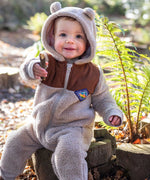A child sitting on a log wearing the Frugi Cord ted fleecy snuggle suit .
