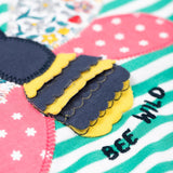 A super close up of the bee applique on the front of the Frugi Theresa top with dragon green coloured stripe and bee design.