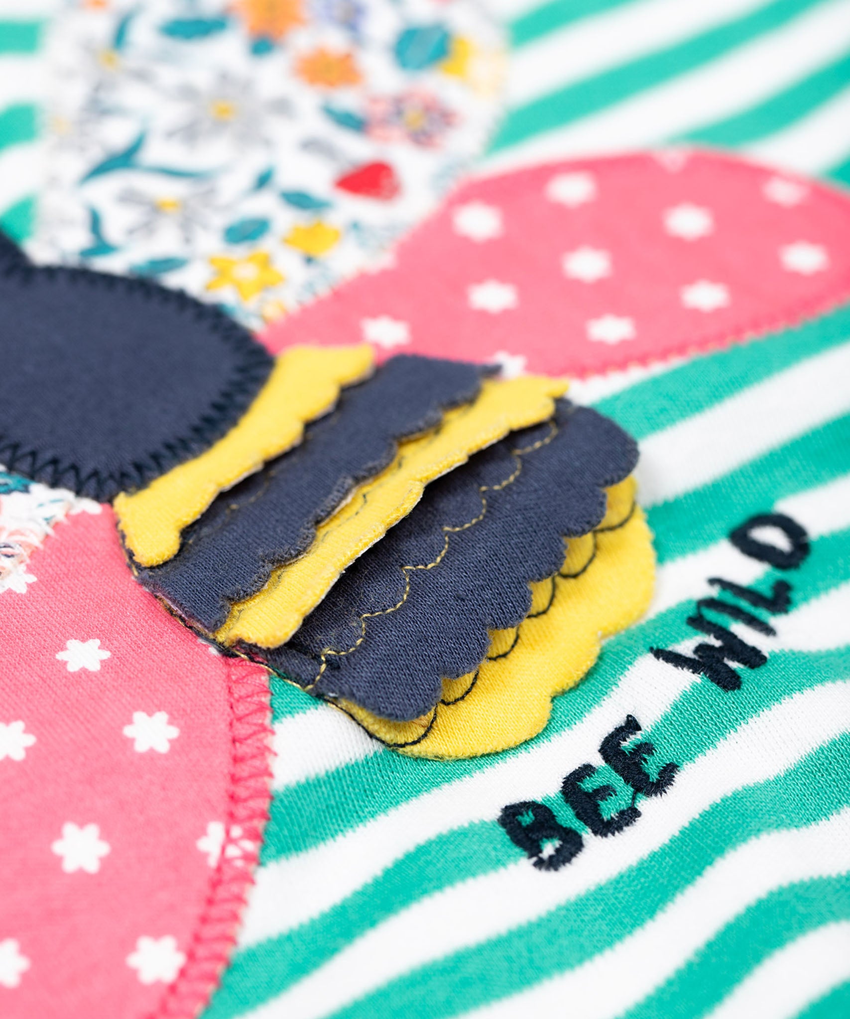 A super close up of the bee applique on the front of the Frugi Theresa top with dragon green coloured stripe and bee design.