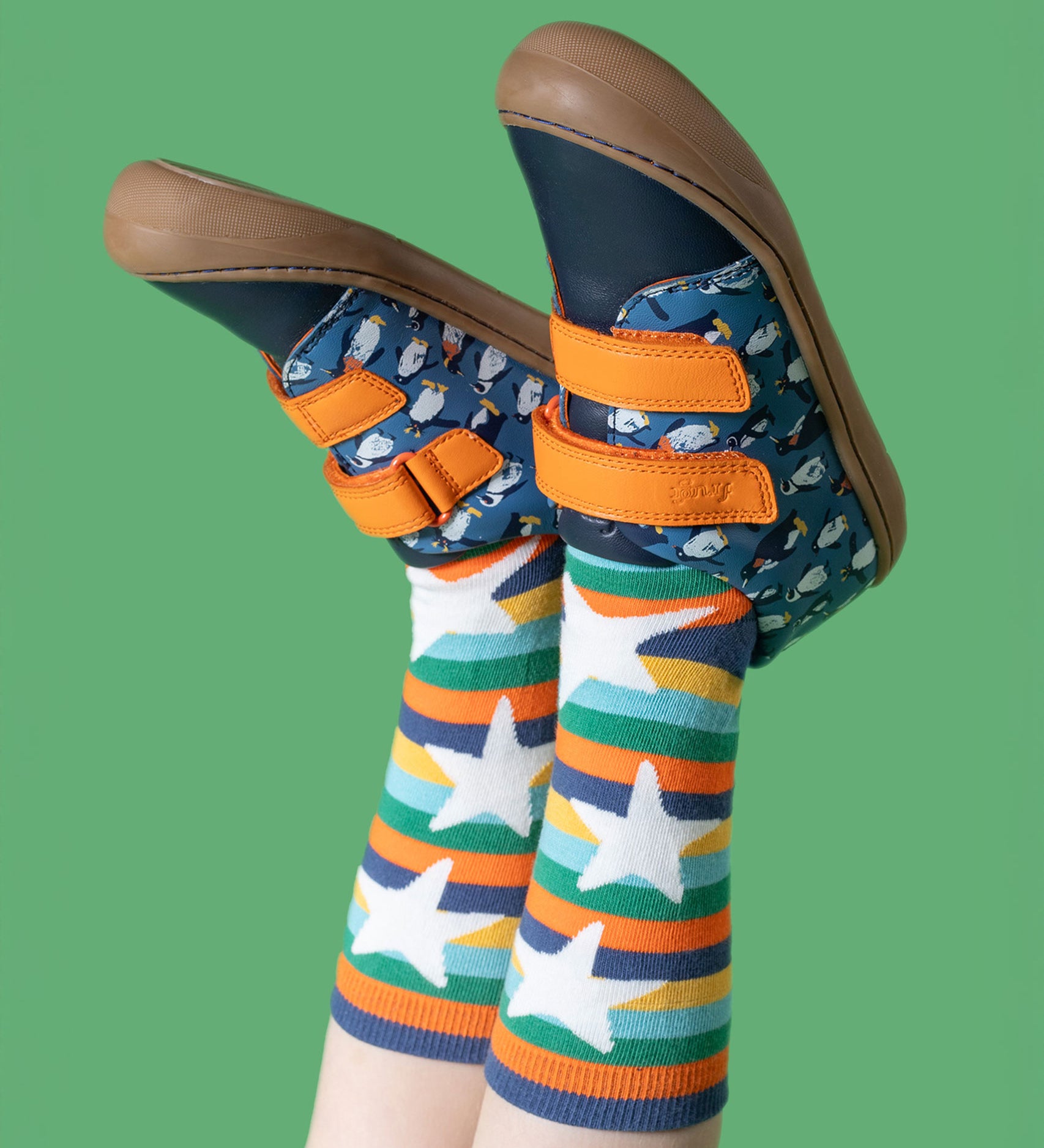 A child wearing the Frugi Penguin Print Tide Low Top velcro closure leather children's shoes with Frugi rainbow striped star socks.