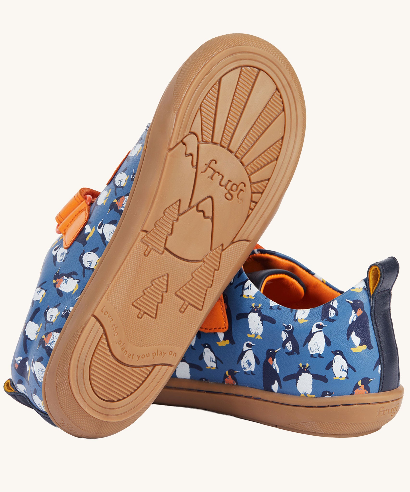 A view of the rubber soles on the Frugi Penguin Print Tide Low Top velcro closure leather children's shoes. The sole features the Frugi logo text in the middle of a mountain-scape scene with the words love the plant you play on featured within the design. 
