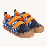 Frugi Penguin Print Tide Low Top velcro closure leather children's shoes. The side and back panels have a blue background with an all over penguin print, the front panel is a solid navy blue colour with contrasting orange coloured straps and lining. 