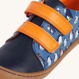 A close up of the orange coloured closure strips on the Frugi Penguin Print Tide Low Top velcro closure leather children's shoes. 