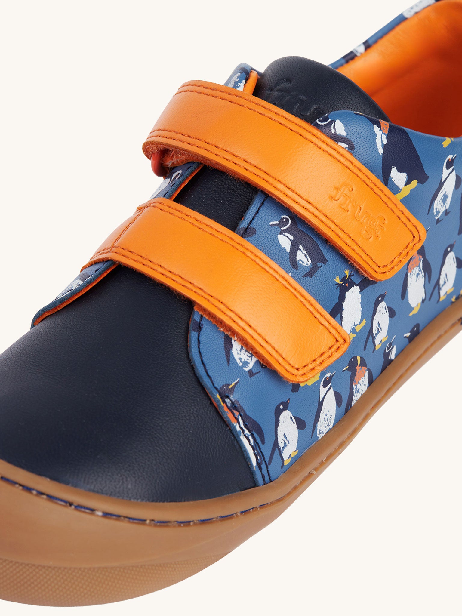A close up of the orange coloured closure strips on the Frugi Penguin Print Tide Low Top velcro closure leather children's shoes. 