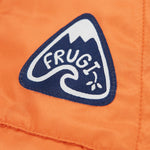 A close up of the Frugi toasty trail reversible jacket showing the brand patch stitched on the side pocket on orange post consumer recycled polyester fabric