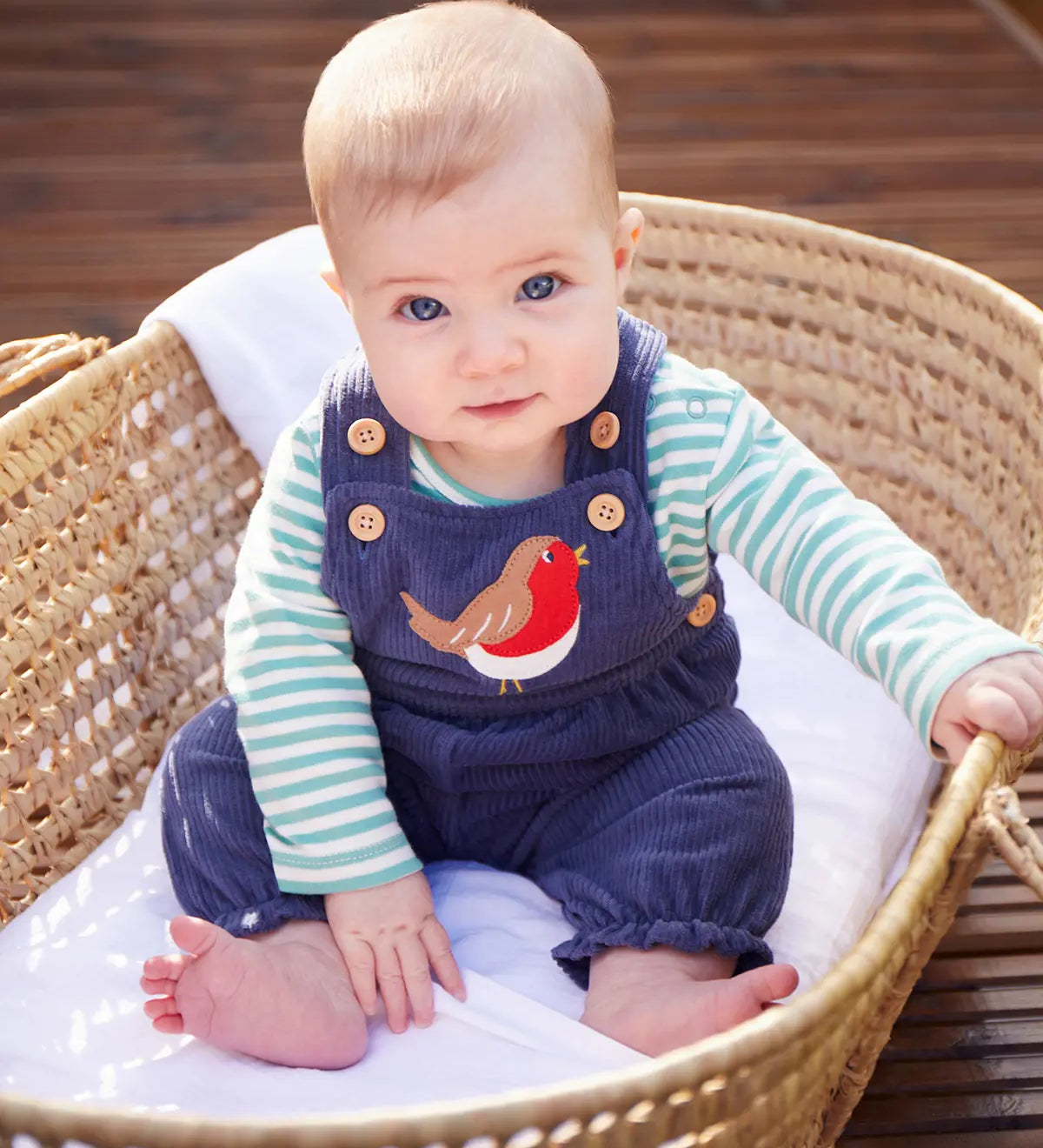 Baby sitting up wearing the Frugi veryan organic cotton navy cord dungaree baby outfit with long sleeve green and white striped bodysuit.