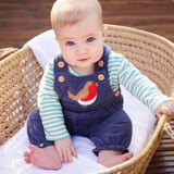 Baby sitting up wearing the Frugi veryan organic cotton navy cord dungaree baby outfit with long sleeve green and white striped bodysuit.