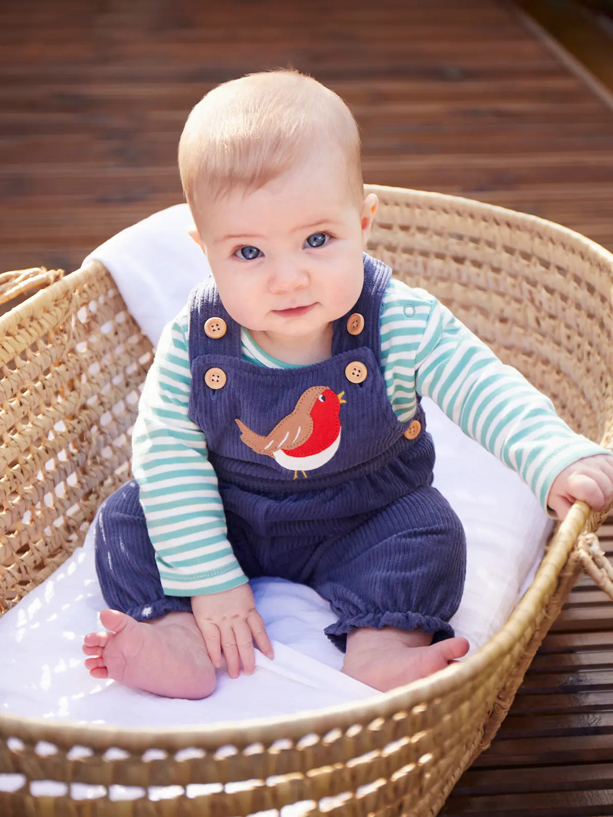 Baby sitting up wearing the Frugi veryan organic cotton navy cord dungaree baby outfit with long sleeve green and white striped bodysuit.
