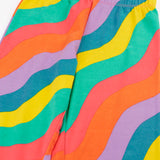 Close up of the Frugi organic cotton wide leg rainbow ric rac pattern children's trousers showing the colourful wavy pattern and elasticated waistband. 