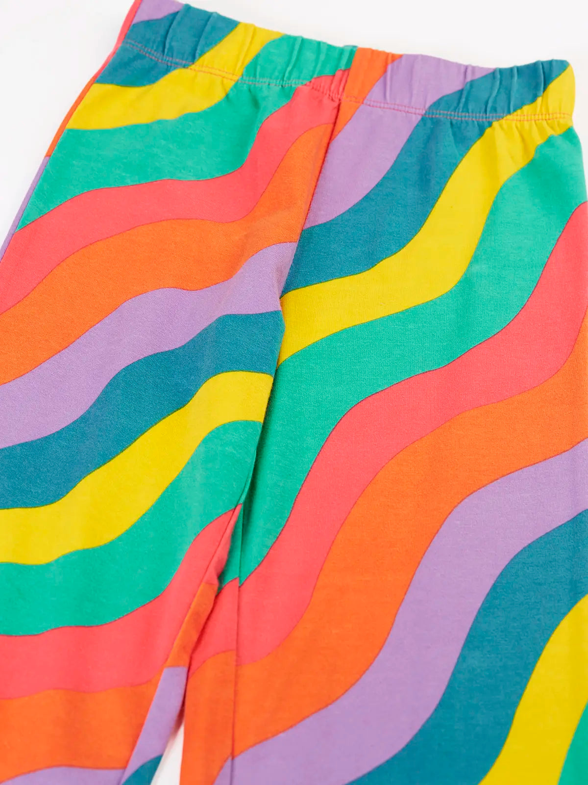 Close up of the Frugi organic cotton wide leg rainbow ric rac pattern children's trousers showing the colourful wavy pattern and elasticated waistband. 