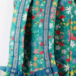 A close up of the Frugi kids trail blazing backpack in wild woods. Showing the shoulder strap detail and blue chest buckle connecting the shoulder straps