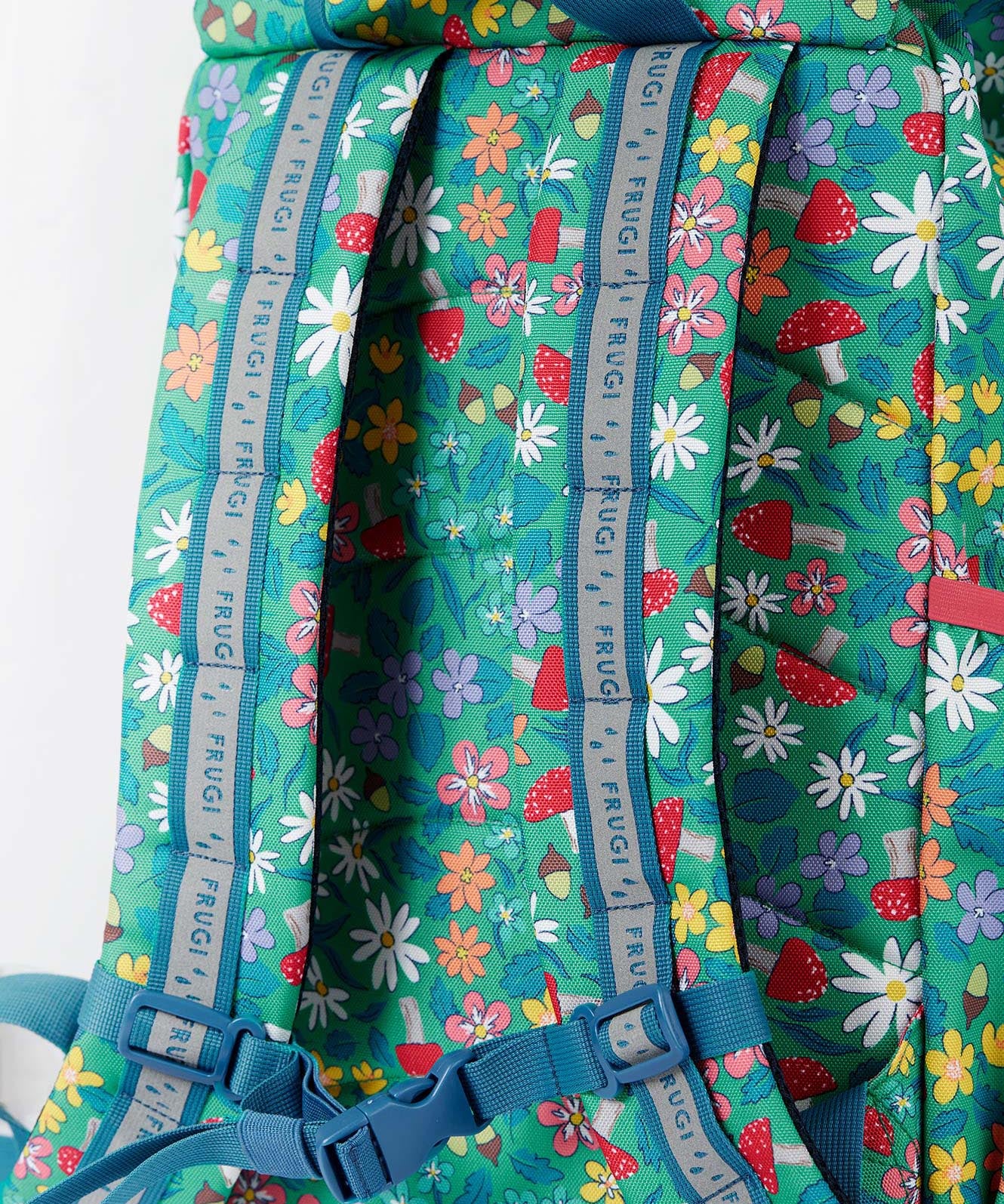 A close up of the Frugi kids trail blazing backpack in wild woods. Showing the shoulder strap detail and blue chest buckle connecting the shoulder straps