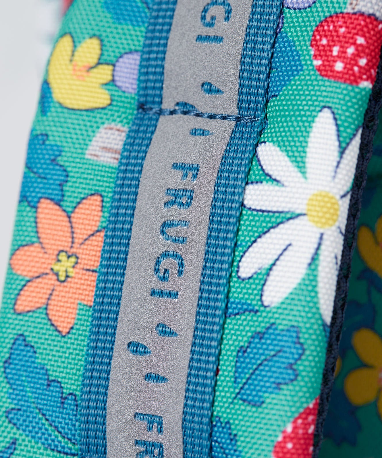 A close up of the shoulder strap on the Frugi kids trail blazing backpack in wild woods. Showing the reflective strip running down the strap
