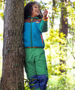 A child wearing the Frugi Wilderness green trousers with navy blue coloured knee patches with a Frugi colour block fleece. 