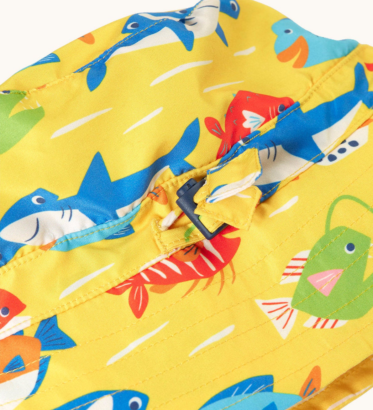 Close up of the adjustable toggle on the front of the Frugi yellow adjustable swim hat with fish and shark sealife design.