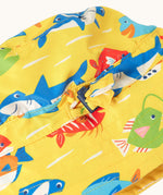 Close up of the adjustable toggle on the front of the Frugi yellow adjustable swim hat with fish and shark sealife design.