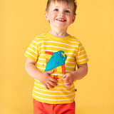A child facing the camera smiling looking up wearing a Frugi interactive ray applique yellow breton stripe organic cotton short sleeved T-Shirt with orange coloured shorts. 