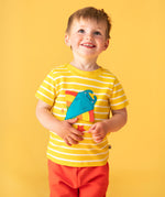A child facing the camera smiling looking up wearing a Frugi interactive ray applique yellow breton stripe organic cotton short sleeved T-Shirt with orange coloured shorts. 