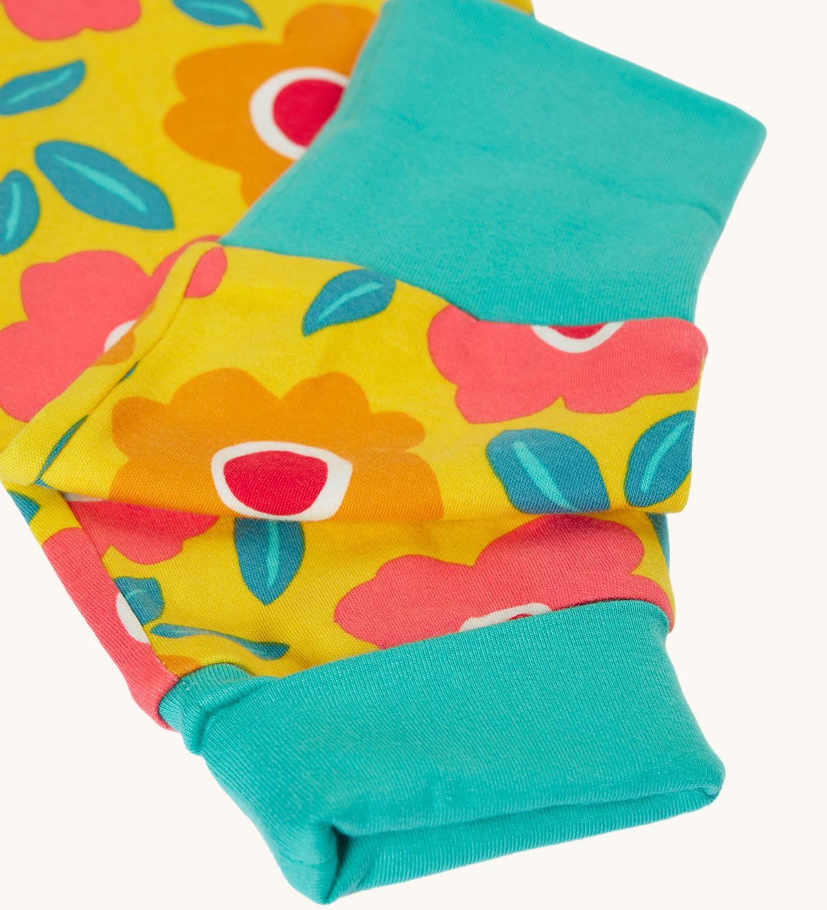 A close up of the turquoise coloured grow with me cuffs on the Frugi zelah zip up all in one with a floral fields print design. A bright yellow organic cotton all in one with pink and orange flowers all over.