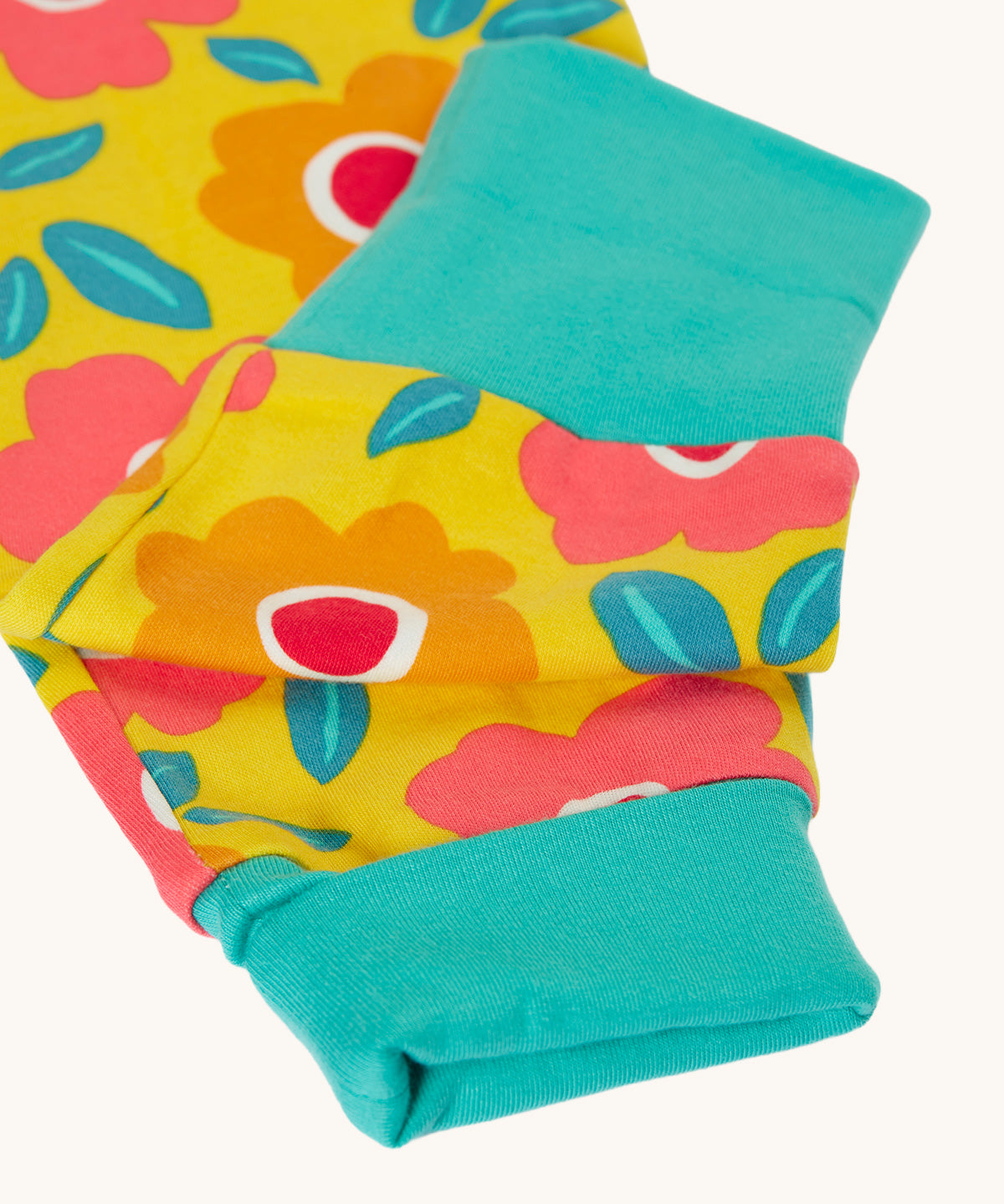 A close up of the turquoise coloured grow with me cuffs on the Frugi zelah zip up all in one with a floral fields print design. A bright yellow organic cotton all in one with pink and orange flowers all over.