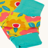 A close up of the turquoise coloured grow with me cuffs on the Frugi zelah zip up all in one with a floral fields print design. A bright yellow organic cotton all in one with pink and orange flowers all over.