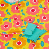 A close up of the front of the Frugi zelah zip up all in one with a floral fields print design. A bright yellow organic cotton all in one with pink and orange flowers all over. The sleeves are shown with the cuffs turned up.  