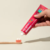 Adult hand squeezing a tube of Georganics fluoride free strawberry hydroxyapatite toothpaste on a toothbrush