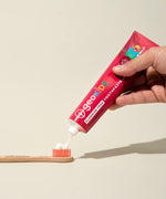 Adult hand squeezing a tube of Georganics fluoride free strawberry hydroxyapatite toothpaste on a toothbrush