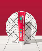 Tube of Georganics strawberry hydroxyapatite toothpaste tube on a tile style floor and matching red background.