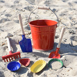A collection of Glückskäfer Metal outdoor toys and children's tools placed on the sand on a beach.