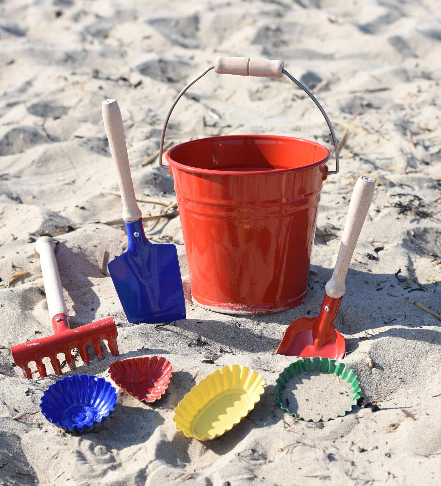 A collection of Glückskäfer Metal outdoor toys and children's tools placed on the sand on a beach.