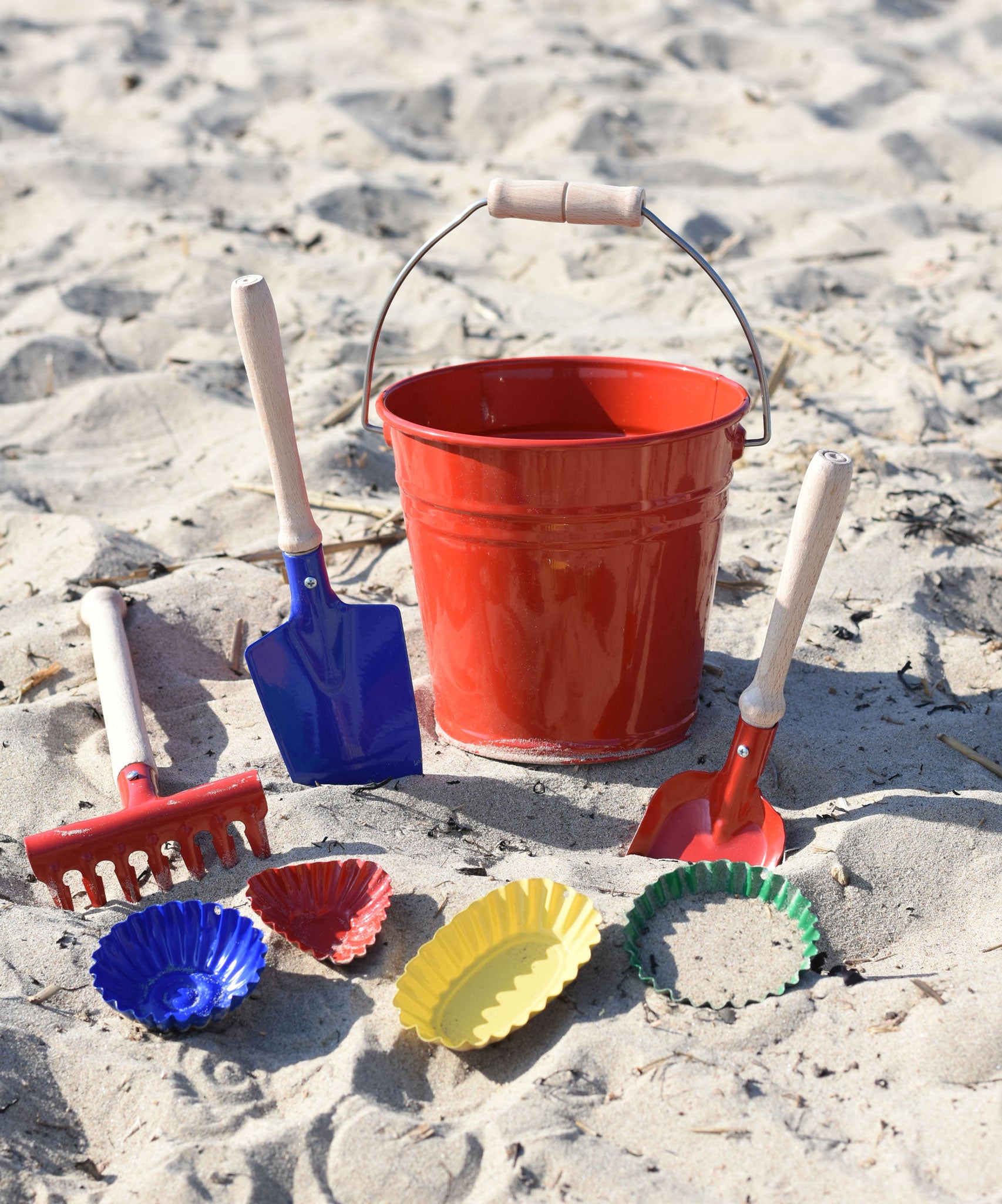 A collection of Glückskäfer Metal outdoor toys and children's tools placed on the sand on a beach.