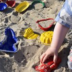 A child placing a red teddy shaped mould in the sand surrounded by  other shaped moulds in the background.