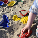 A child placing a red teddy shaped mould in the sand surrounded by  other shaped moulds in the background.