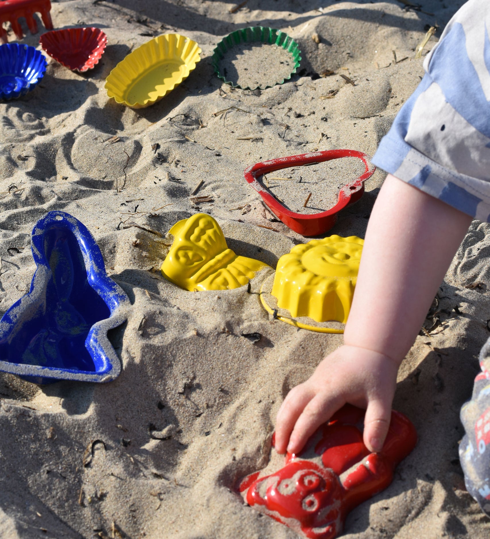 A child placing a red teddy shaped mould in the sand surrounded by  other shaped moulds in the background.